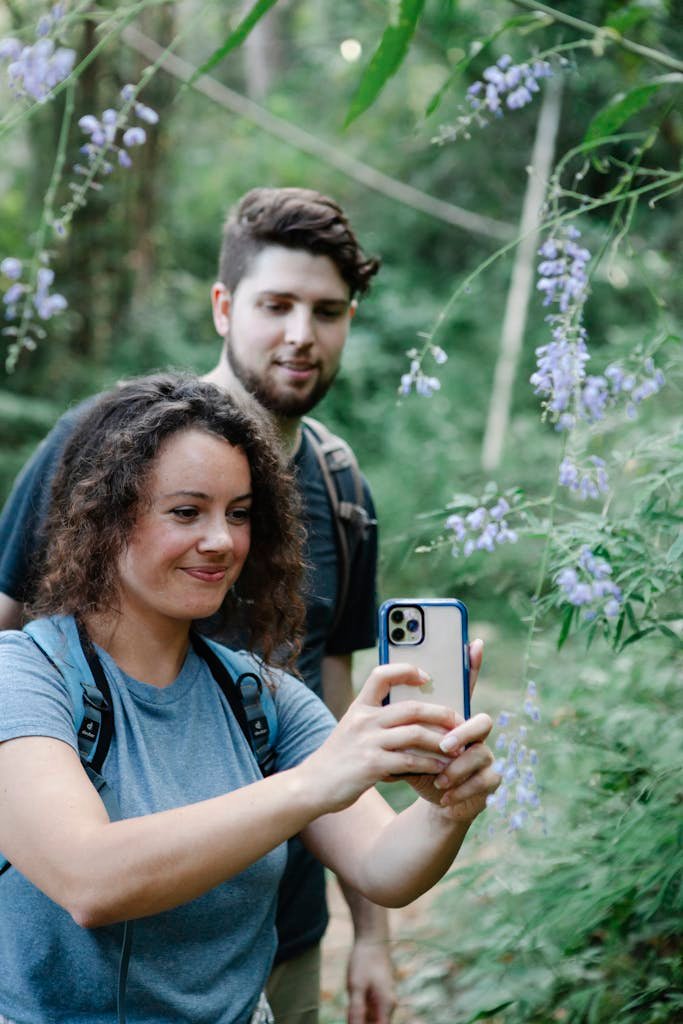 Couple enjoying a hike in the woods, capturing a selfie with blooming flowers around them.